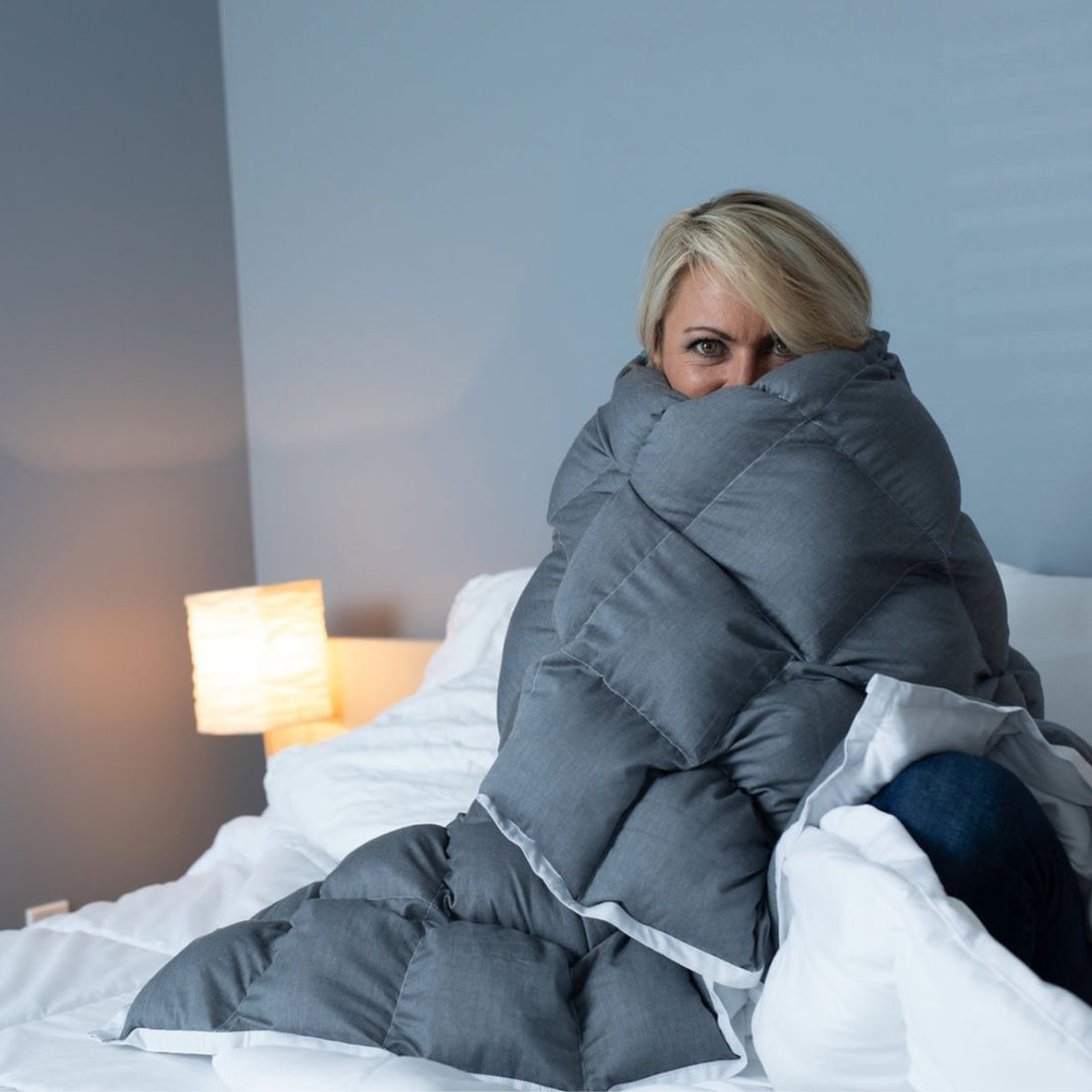 woman wrapped in weighted blanket sitting on bed